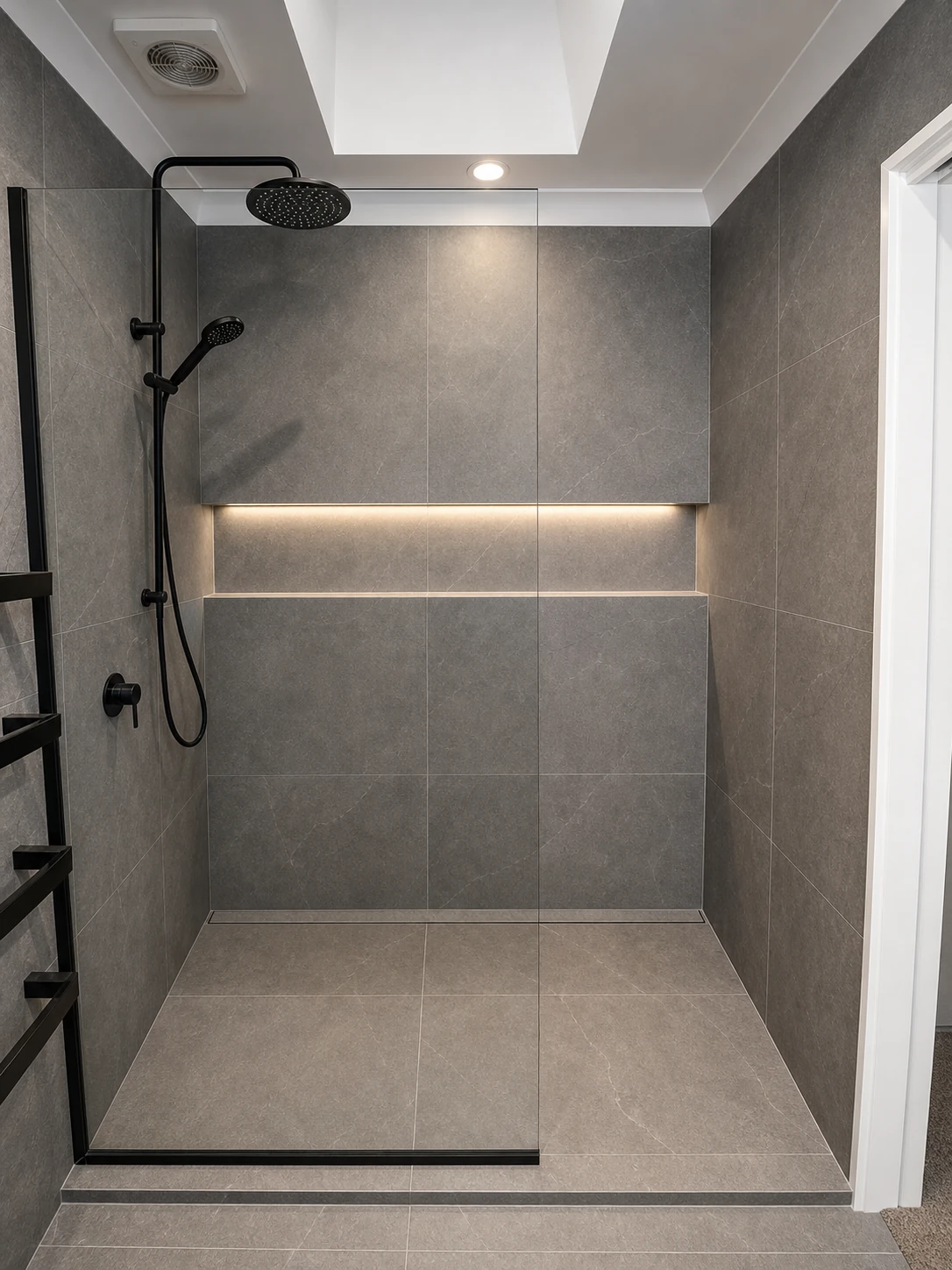 Grey tiled shower with black fittings and glass screen